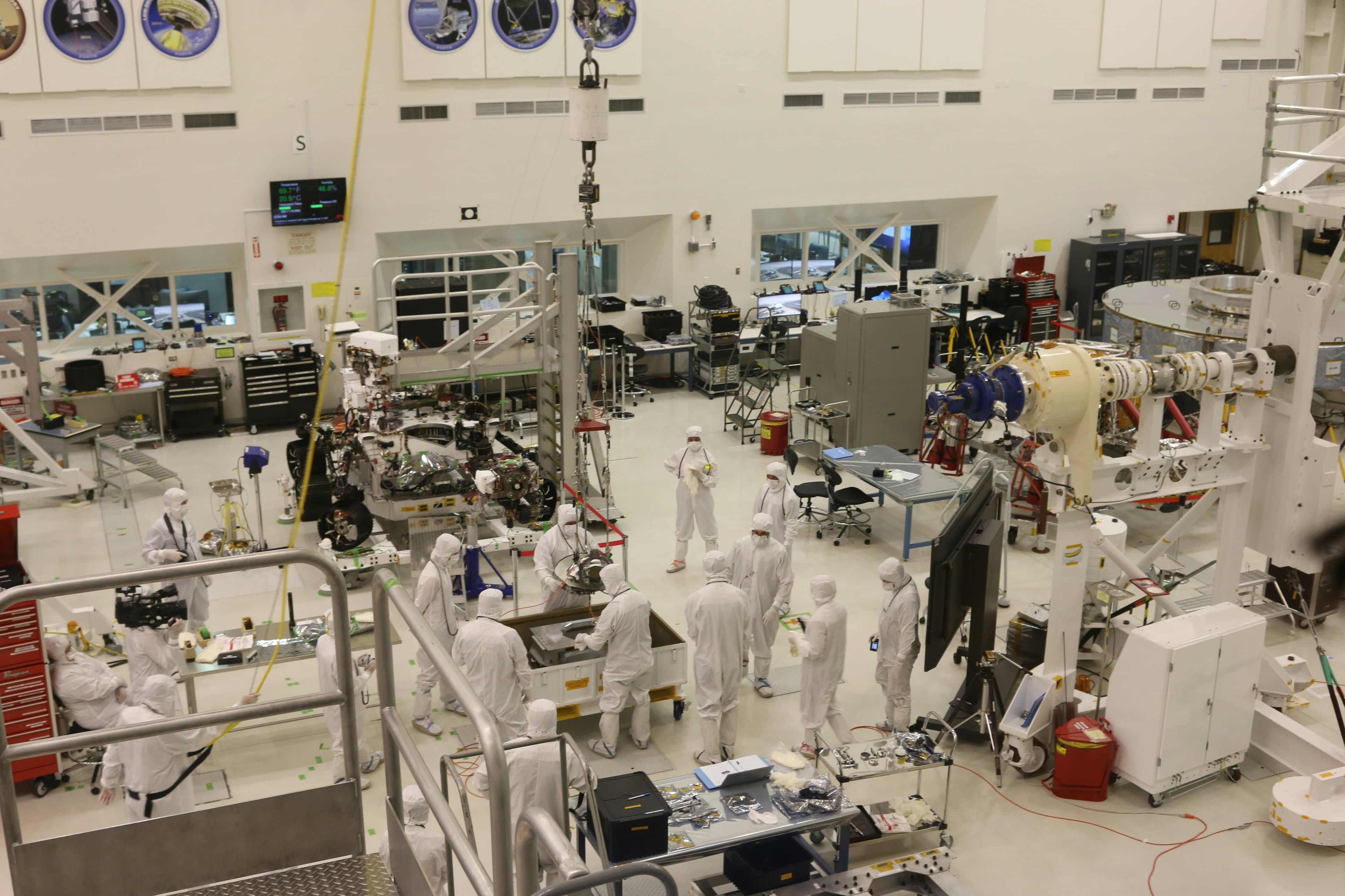 Technicians in cleanroom suits assembling spacecraft hardware in a high-bay facility